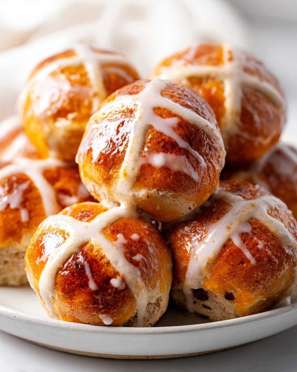 A close-up stack of freshly baked Hot Cross Buns with Orange Glaze, featuring shiny, golden-brown tops and white icing crosses.
