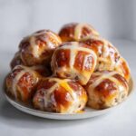 A tempting pile of freshly baked Hot Cross Buns with Orange Glaze, drizzled with a sweet white icing cross.