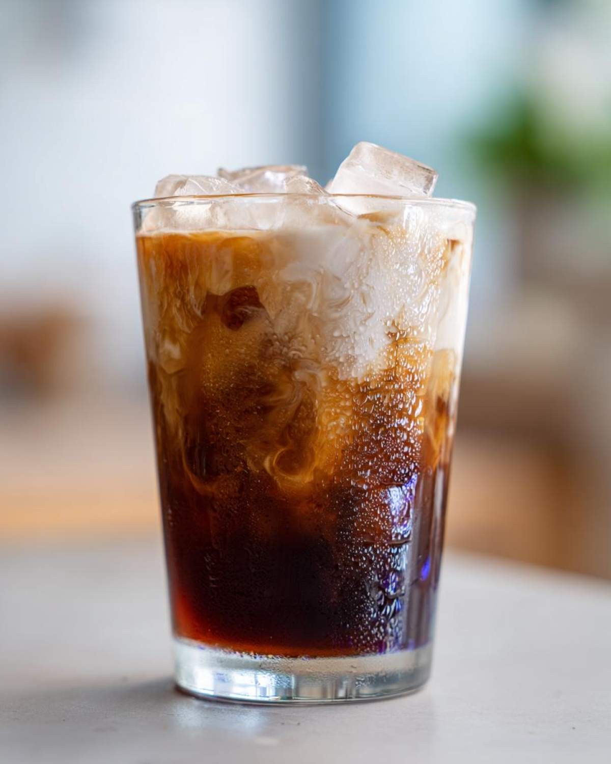 Close-up of a tall glass containing an Iced Lavender Latte, showing dark coffee mixing with creamy white milk and ice cubes.