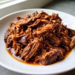 A close-up of richly seasoned, shredded Instant Pot Beef Barbacoa piled high on a white plate.