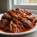 A close-up of saucy, shredded Instant Pot Beef Barbacoa piled high on a white plate.