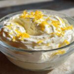 A close-up of creamy Keto Lemon Cheesecake Mousse topped with bright yellow lemon zest in a clear glass bowl.