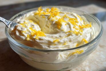 A close-up of creamy Keto Lemon Cheesecake Mousse topped with bright yellow lemon zest in a clear glass bowl.
