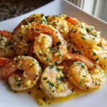 Close-up of succulent Lemon Butter Shrimp with Garlic Flavor, coated in butter sauce and fresh parsley, served on a white plate.