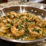Close-up of plump shrimp sizzling in a stainless steel skillet with rich lemon garlic butter sauce and fresh parsley.