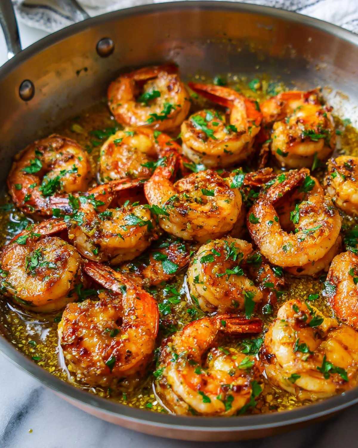 Close-up of juicy shrimp sizzling in a skillet with rich lemon garlic butter sauce and fresh parsley.