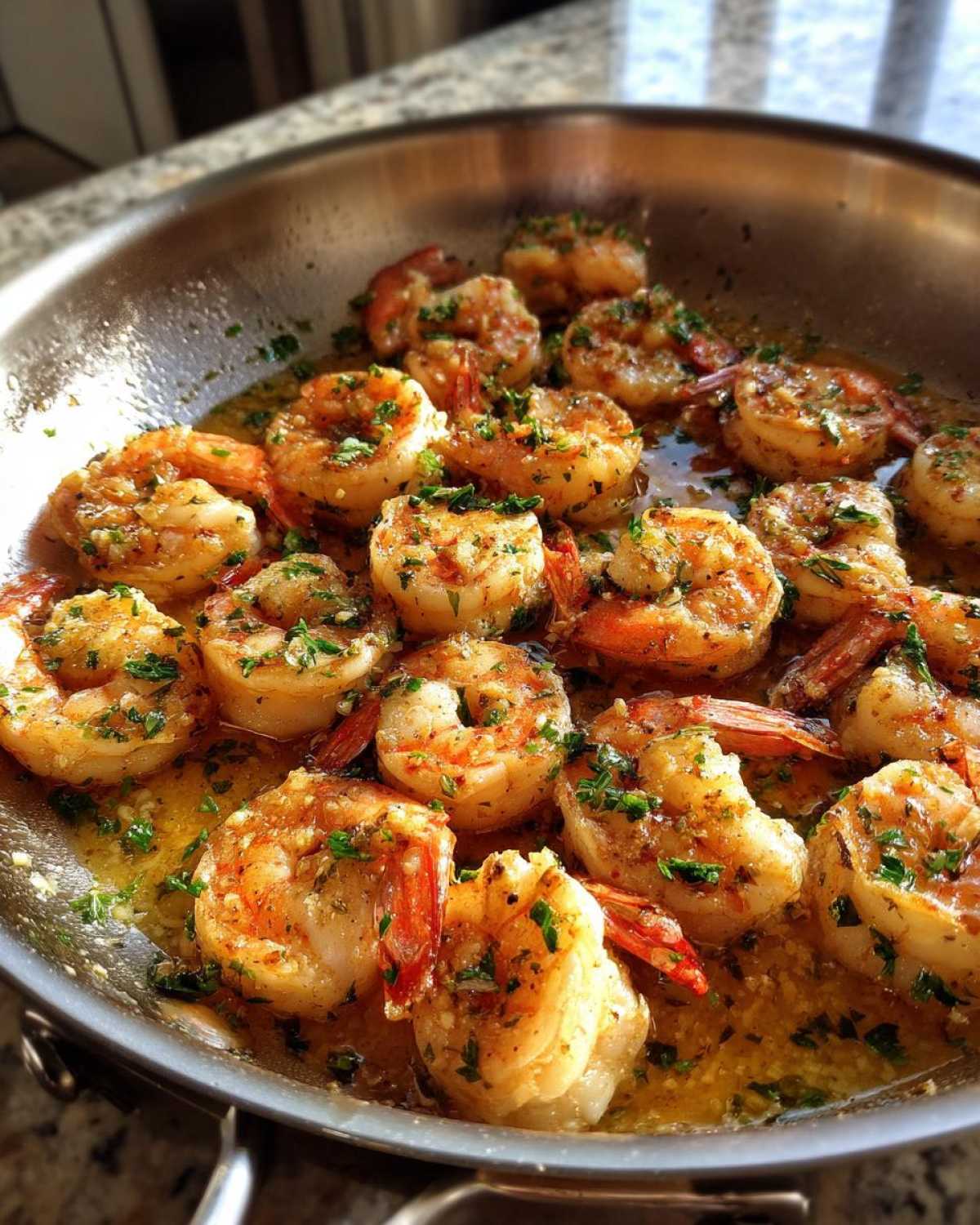 Close-up of plump shrimp sizzling in a stainless steel pan with rich lemon garlic butter sauce and fresh parsley.