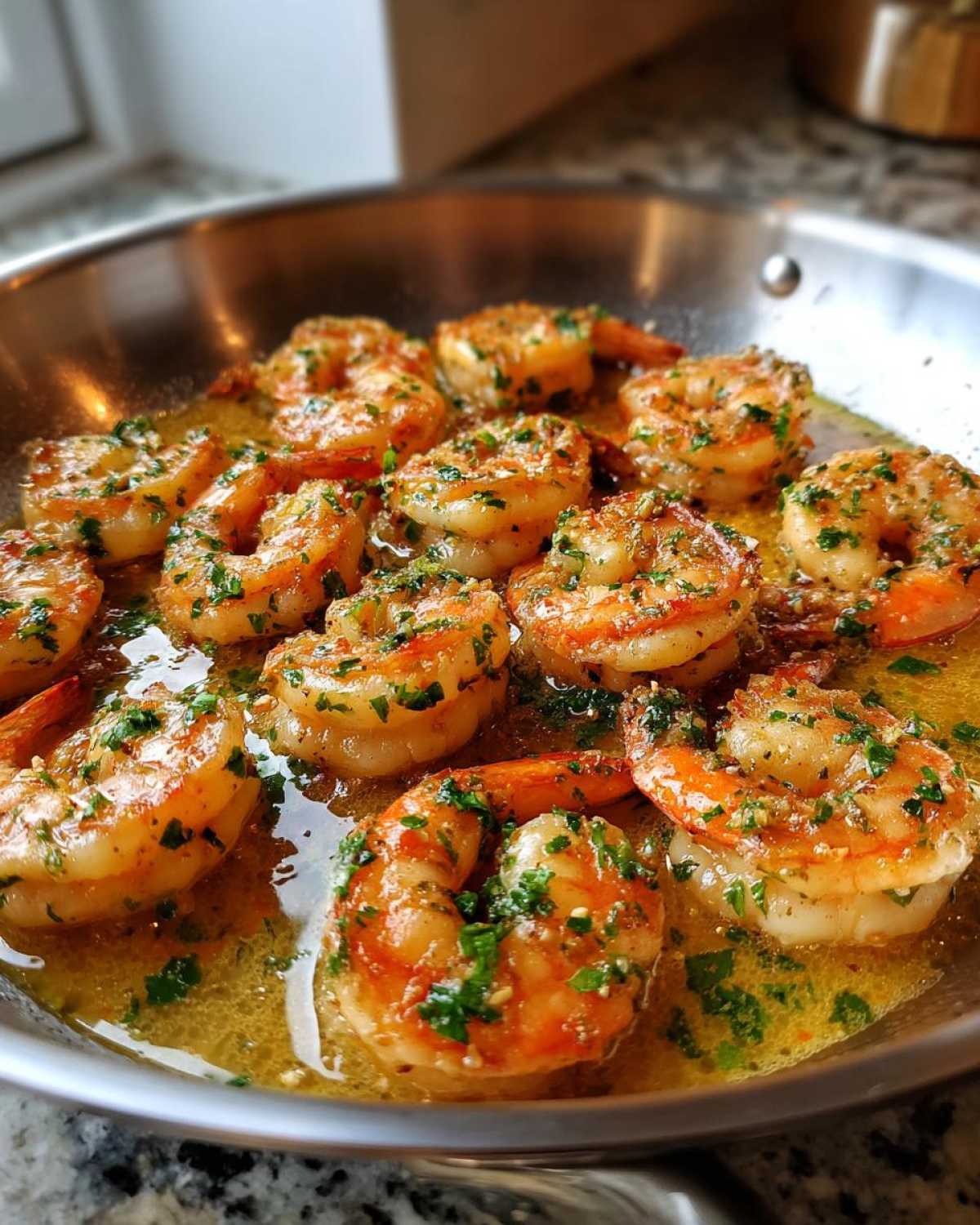 Close-up of succulent shrimp cooking in a stainless steel skillet with rich lemon garlic butter sauce and fresh parsley.