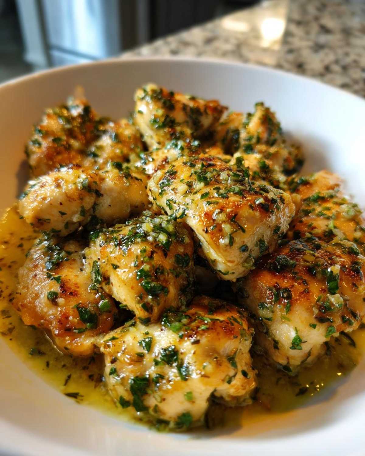 Close-up of golden, pan-seared chicken pieces coated in a bright lemon garlic sauce and fresh herbs.