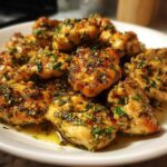 A white plate piled high with golden, pan-seared Lemon Garlic Chicken Skillet pieces coated in a glistening sauce of herbs and garlic.