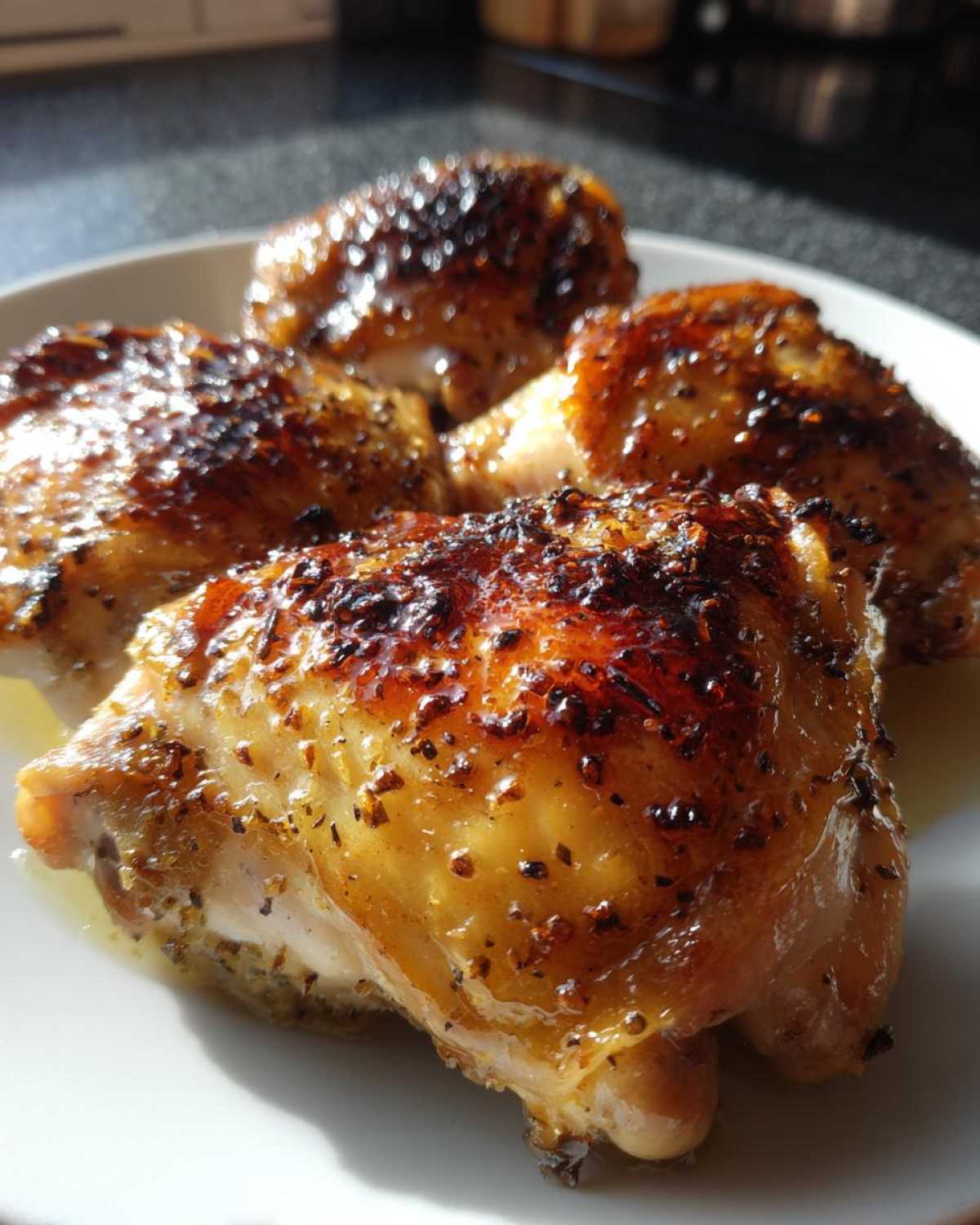 Four perfectly roasted Lemon Garlic Roasted Chicken Thighs with crispy, browned skin resting on a white plate.