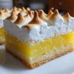 A close-up of a square Lemon Meringue Pie Bars slice showing a shortbread crust, bright yellow lemon filling, and peaked, toasted meringue topping.