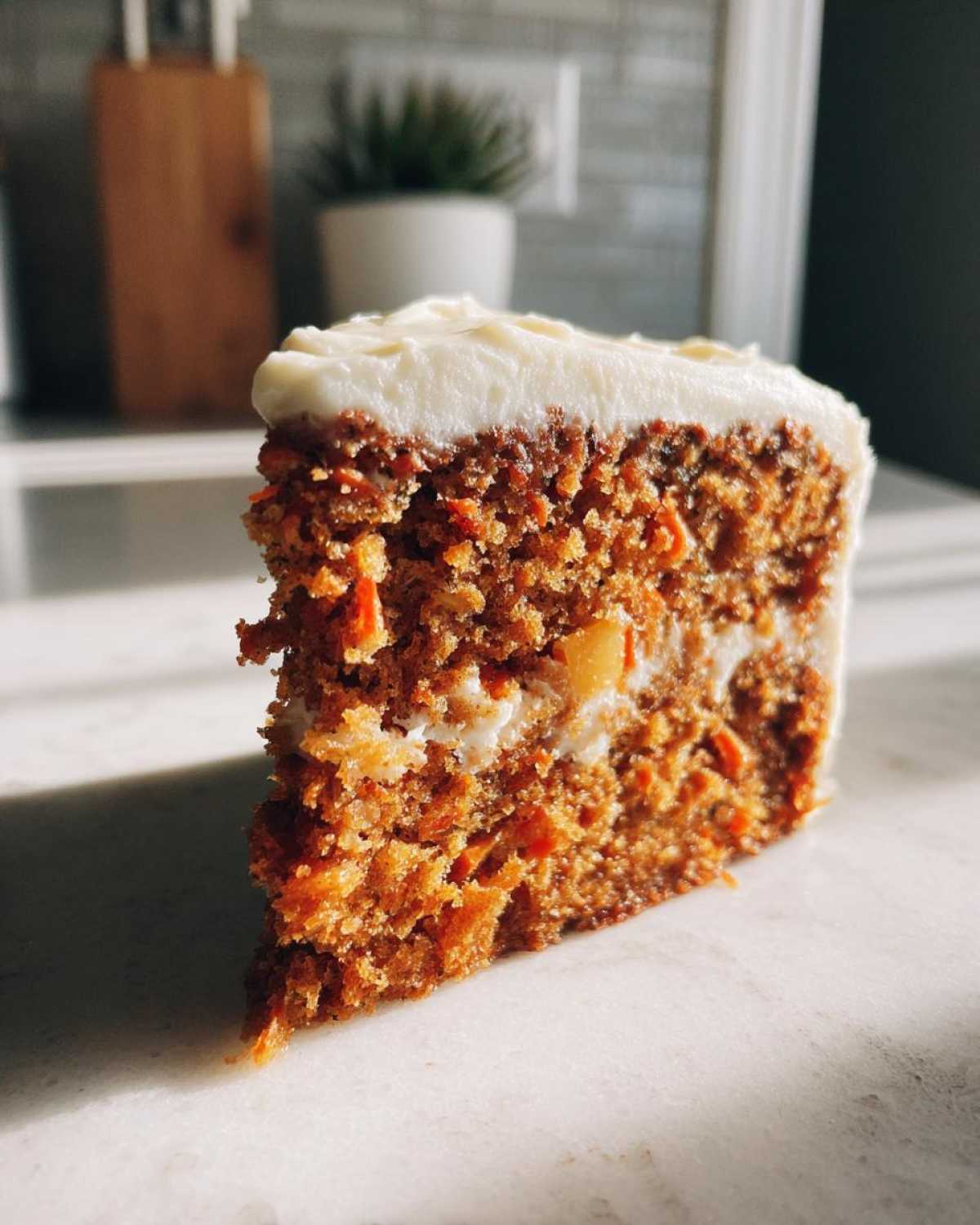 Close-up of a thick slice of Moist Carrot Cake with Cream Cheese Frosting, showing rich texture and bright white icing.