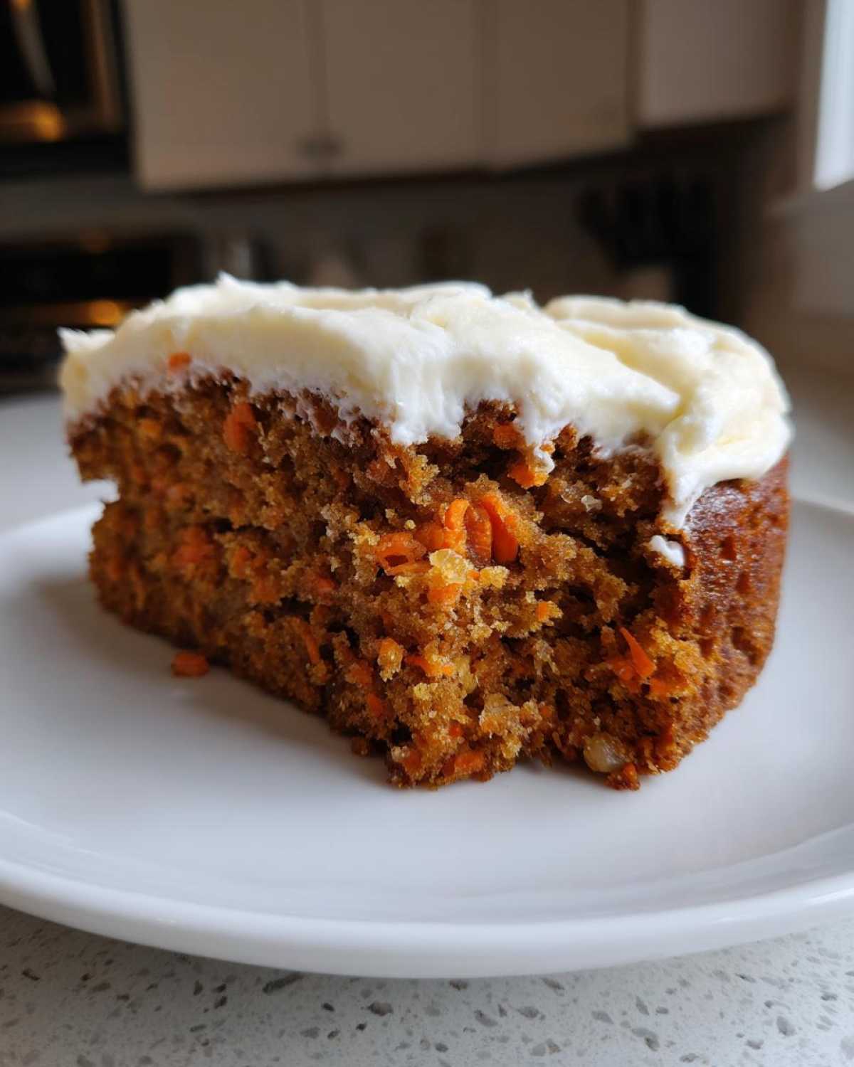 Close-up of a slice of Moist Carrot Cake with Cream Cheese Frosting showing visible shredded carrots in the crumb.