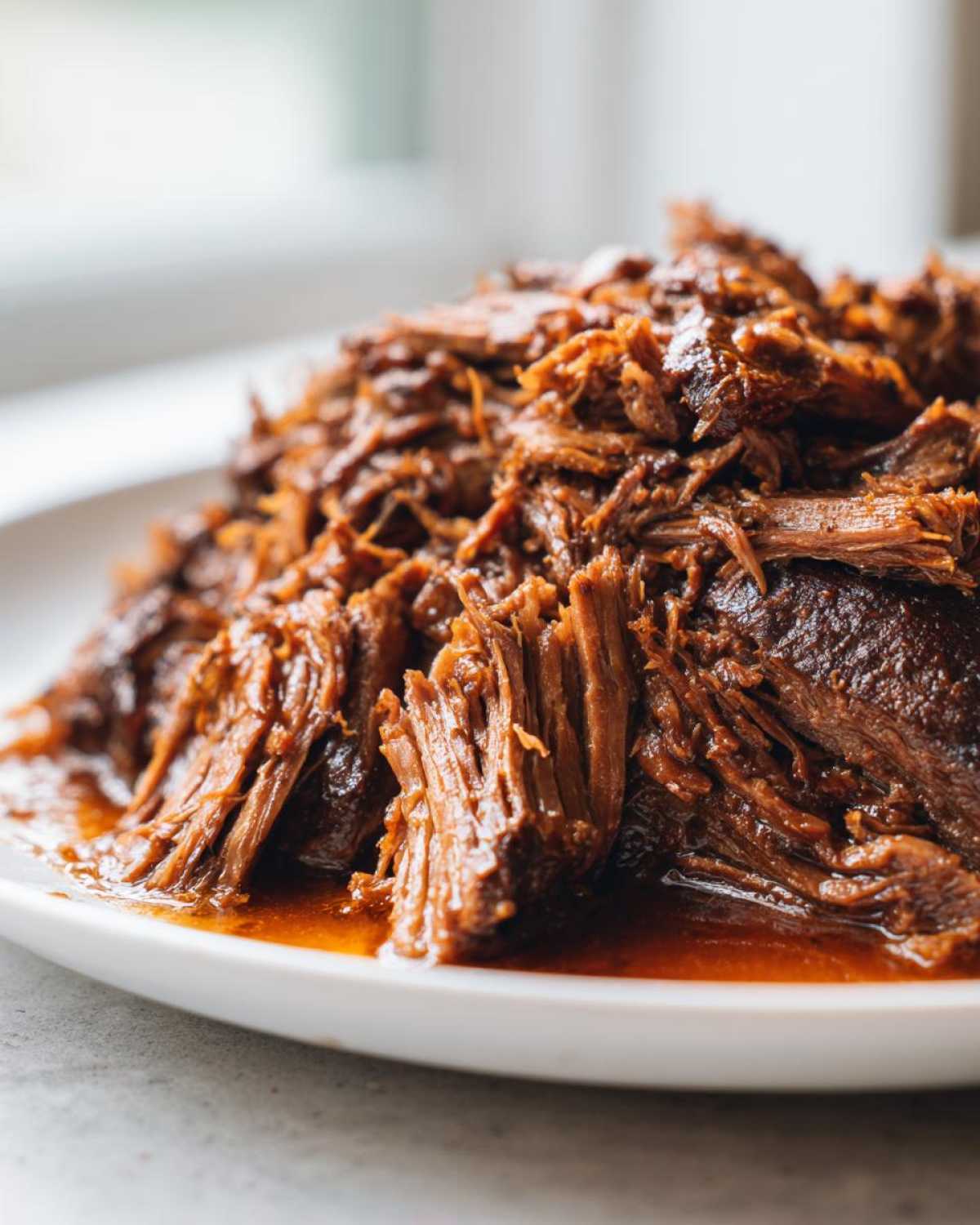 Close-up of tender, shredded Instant Pot Beef Barbacoa coated in rich sauce on a white plate.