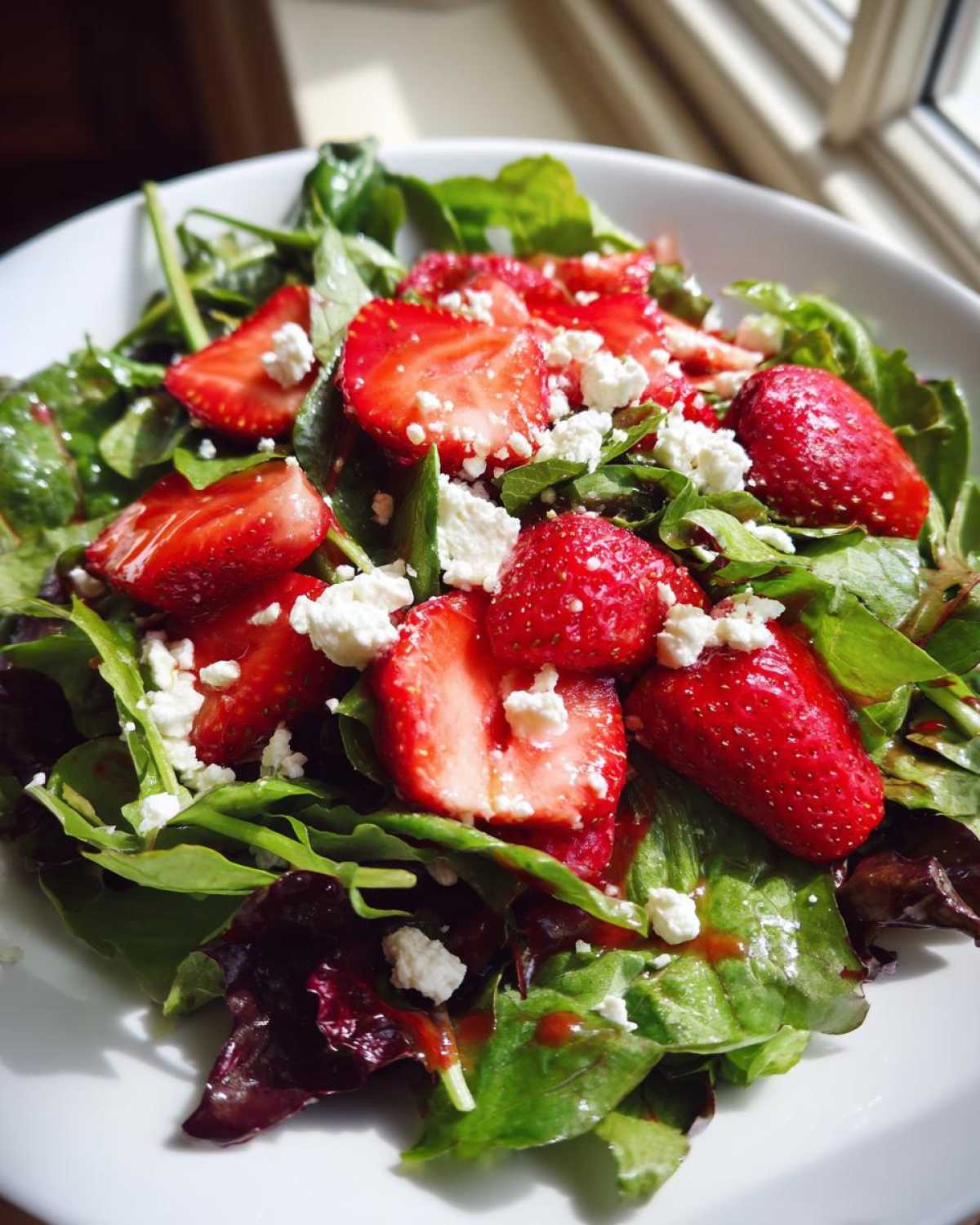 Close-up of a vibrant Spring Mix Salad with Strawberries and Goat Cheese, drizzled with dressing.
