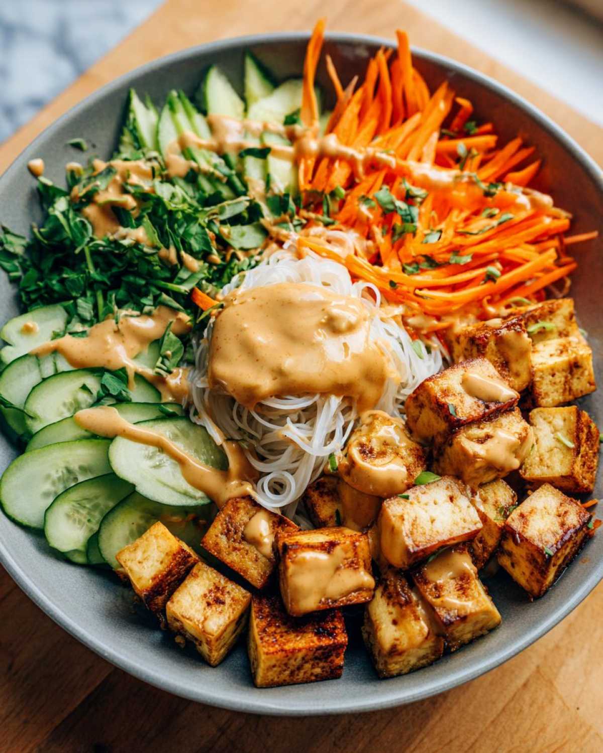 Close-up of a vibrant Spring Roll Bowl with Peanut Sauce, featuring rice noodles, crispy tofu, cucumber, and shredded carrots.