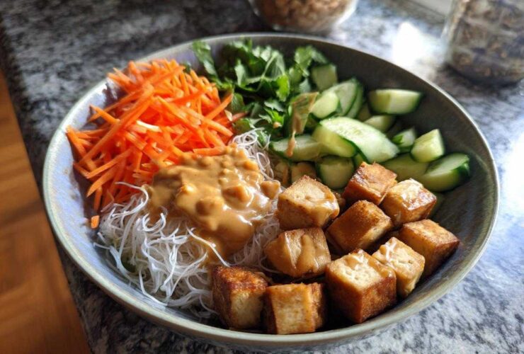 A vibrant Spring Roll Bowl with Peanut Sauce featuring vermicelli noodles, crispy tofu cubes, shredded carrots, cucumbers, and fresh herbs.