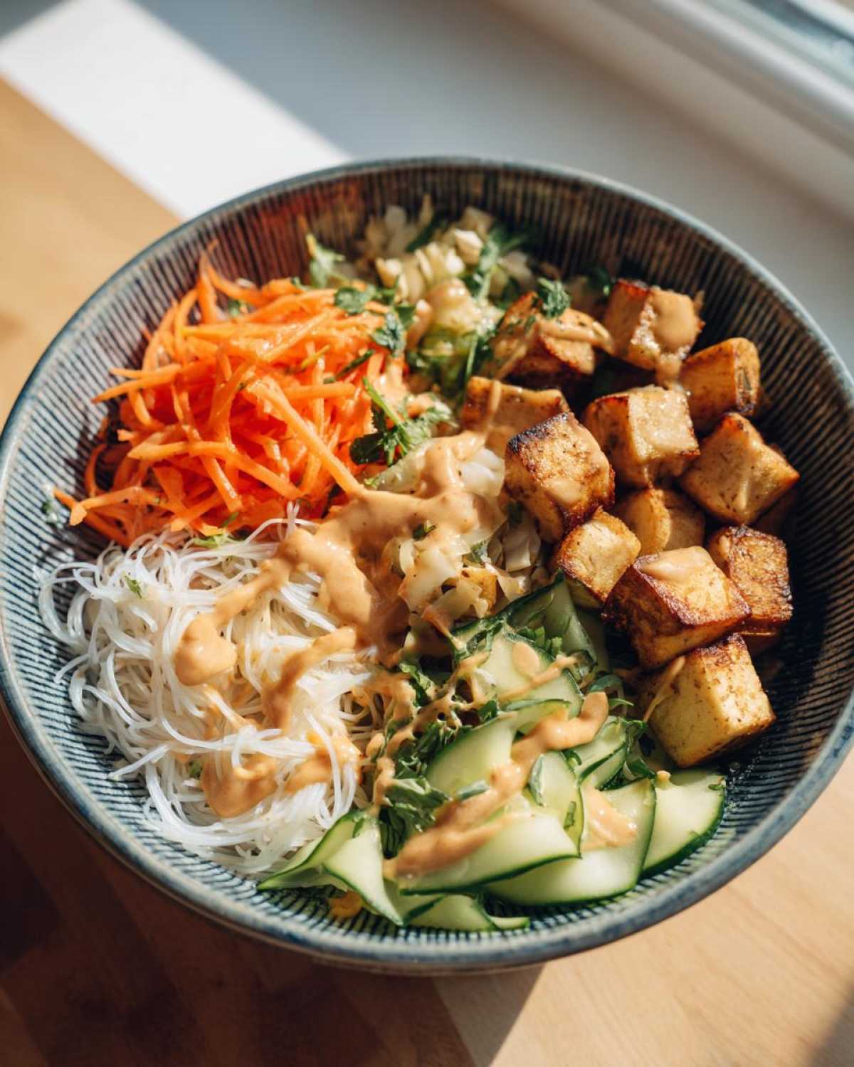 Close-up of a colorful Spring Roll Bowl with Peanut Sauce, featuring rice noodles, crispy tofu, shredded carrots, and cucumber.