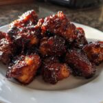 A pile of glistening Sticky BBQ Chicken Bites with deep caramelized edges served on a white plate.