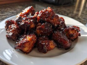 A pile of glistening Sticky BBQ Chicken Bites with deep caramelized edges served on a white plate.