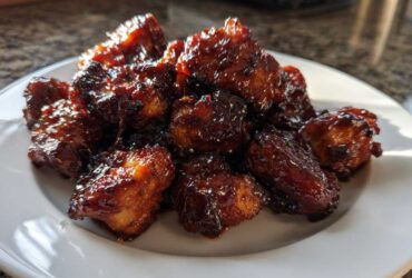 A pile of glistening Sticky BBQ Chicken Bites with deep caramelized edges served on a white plate.