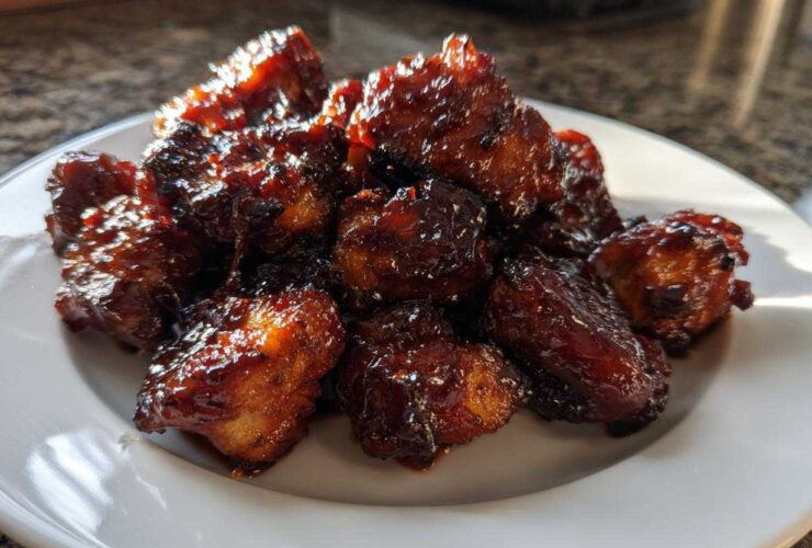 A pile of glistening Sticky BBQ Chicken Bites with deep caramelized edges served on a white plate.