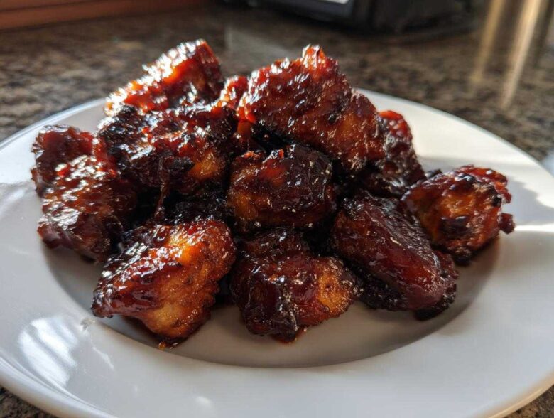 A pile of glistening Sticky BBQ Chicken Bites with deep caramelized edges served on a white plate.