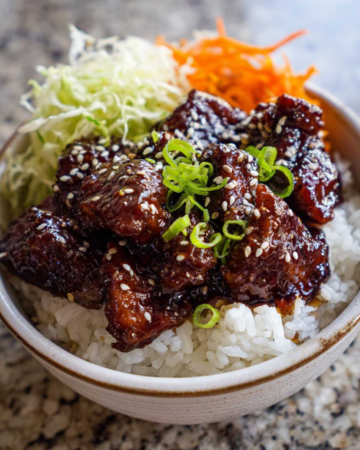 Close-up of a Sticky BBQ Chicken Bowl with Rice, topped with sesame seeds and green onions.