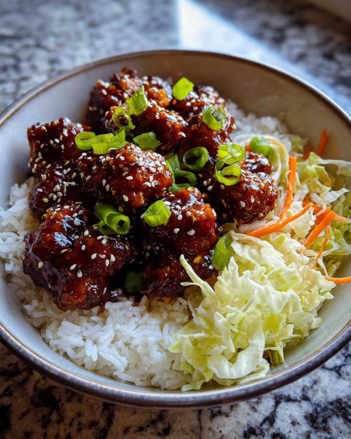 A close-up of a Sticky BBQ Chicken Bowl with Rice, topped with sesame seeds and green onions.