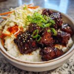 Close-up of a Sticky BBQ Chicken Bowl with Rice, topped with sesame seeds and green onions.