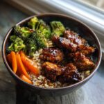 A close-up of a Sticky BBQ Chicken Bowl with Veggies, featuring glazed chicken pieces over brown rice with roasted broccoli and carrots.