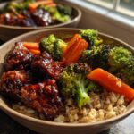 Close-up of a Sticky BBQ Chicken Bowl with Veggies featuring glazed chicken pieces, roasted broccoli, carrots, and brown rice.