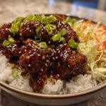 A close-up of a Sticky BBQ Chicken Bowl with Rice, featuring glazed chicken pieces over white rice with slaw and green onions.