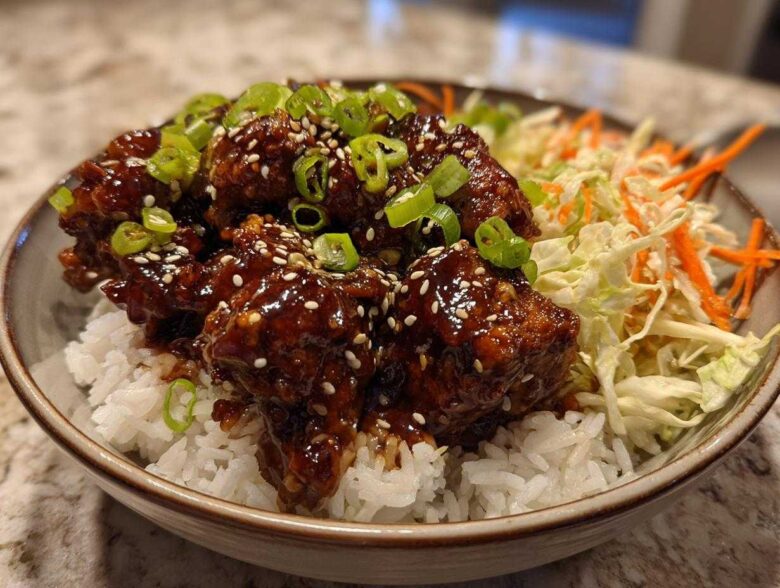 A close-up of a Sticky BBQ Chicken Bowl with Rice, featuring glazed chicken pieces over white rice with slaw and green onions.