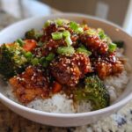 Close-up of a Sticky Orange Chicken Bowl with rice, broccoli, carrots, and sesame seeds.