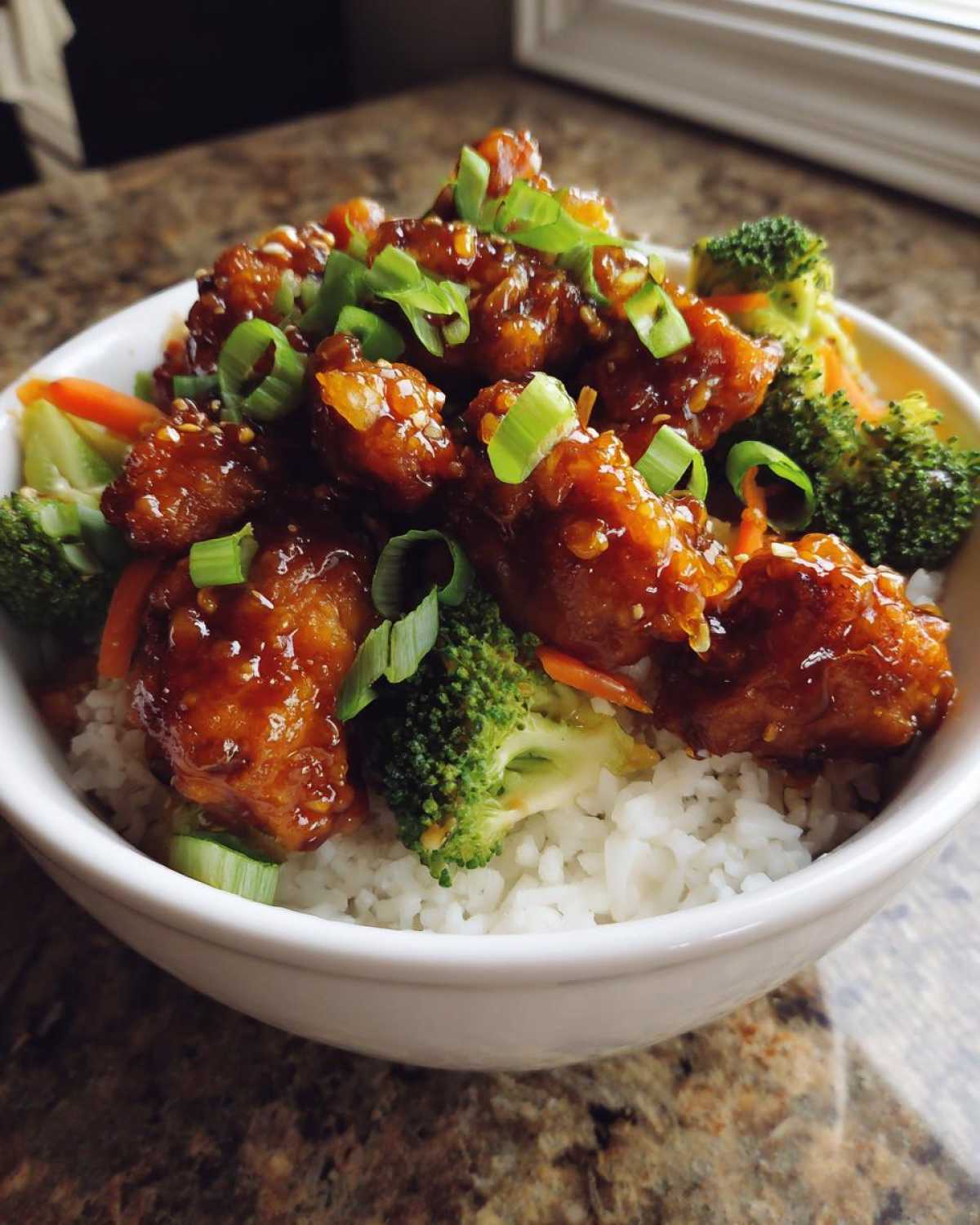 Close-up of a Sticky Orange Chicken Bowl with glossy orange chicken pieces over rice and steamed broccoli.