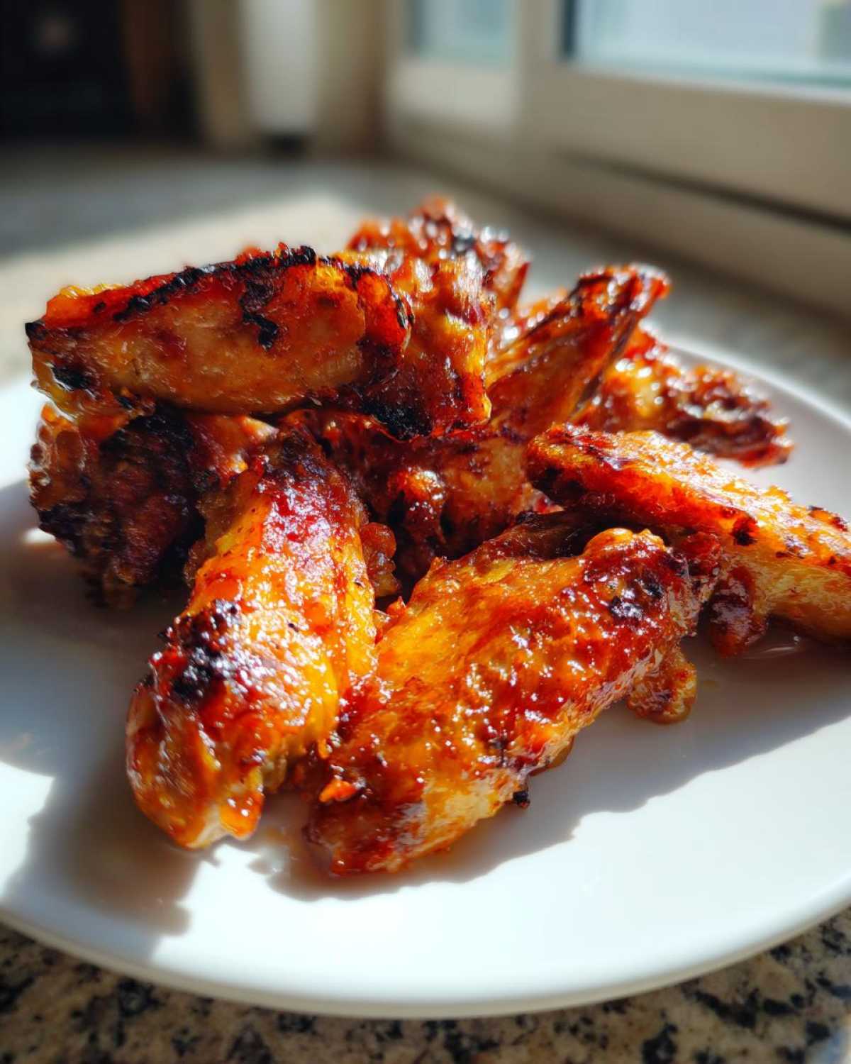 Close-up of perfectly glazed and slightly charred Sticky Orange Chicken Wings piled on a white plate.
