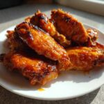 Close-up of several Sticky Orange Chicken Wings with Honey Glaze glistening under sunlight on a white plate.