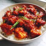 Close-up of Sticky Sweet Chili Chicken Skillet pieces coated in glossy red sauce served over white rice, garnished with green onions.