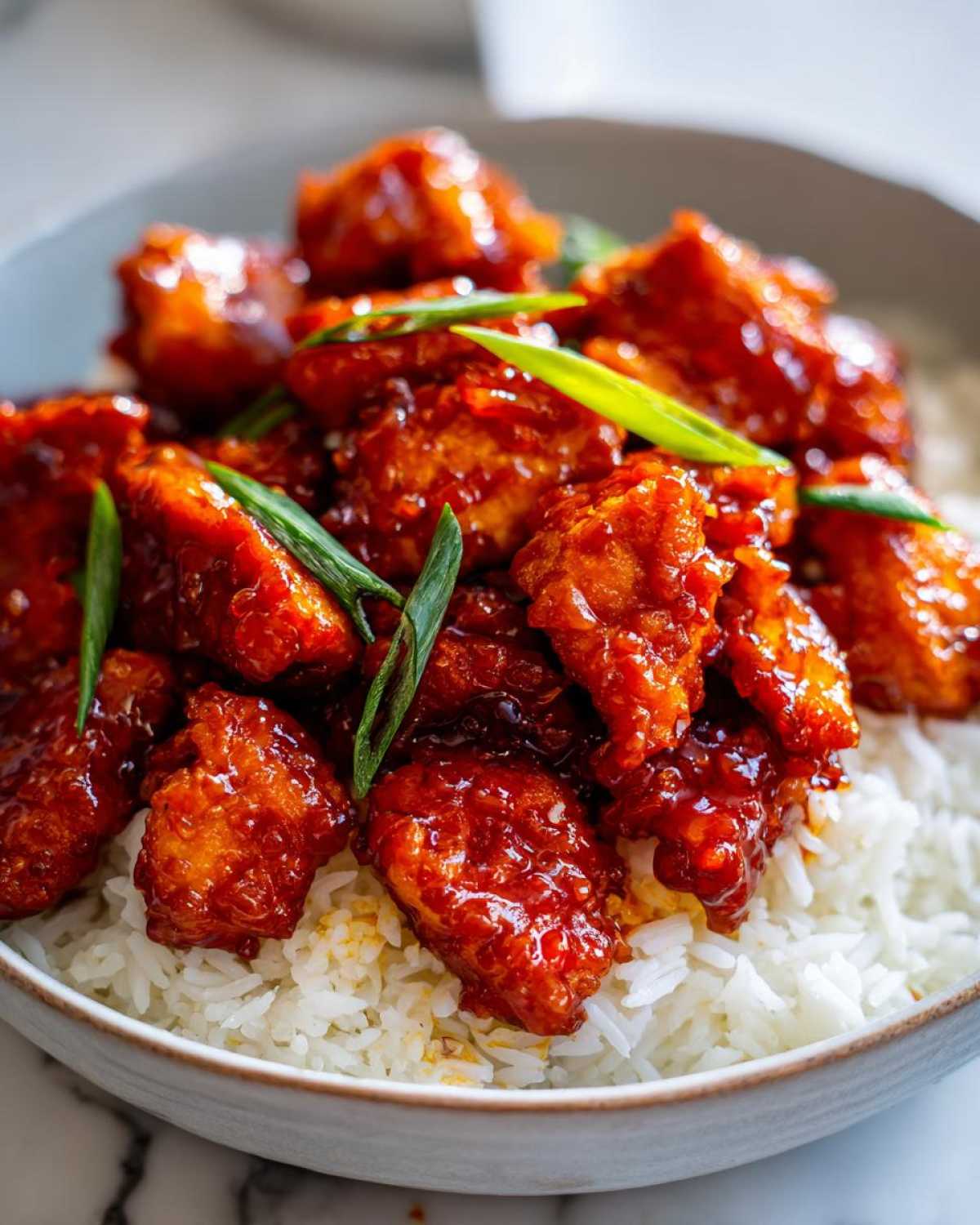 Close-up of crispy chicken pieces coated in a glossy red sauce, served over white rice, garnished with green onions, for Sticky Sweet Chili Chicken Skillet.