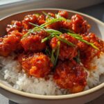 Close-up of Sticky Sweet Chili Chicken Skillet pieces coated in glossy red sauce served over white rice and garnished with green onions.