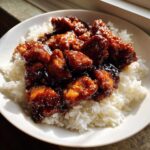 Close-up of Sticky Sweet Soy Chicken pieces coated in a dark, glossy sauce served over white rice.