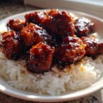 Close-up of Sticky Sweet Soy Chicken pieces coated in dark, glossy sauce served over a bed of fluffy white rice.