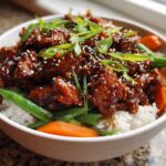 A close-up of a white bowl filled with Sticky Teriyaki Chicken Bowl, featuring glazed chicken over white rice, green beans, carrots, and sesame seeds.