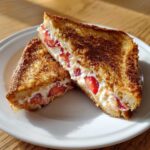 Two halves of golden brown Strawberry Cream Cheese Stuffed French Toast, showing the creamy filling and sliced strawberries.