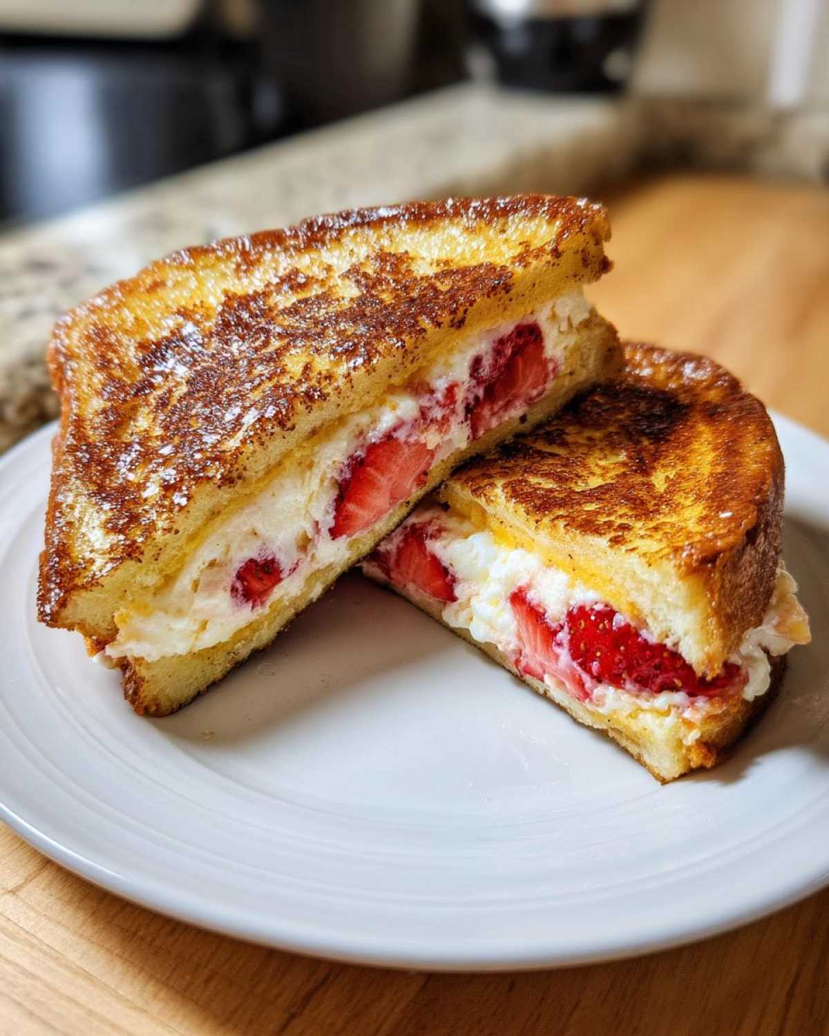 Two halves of golden-brown Strawberry Cream Cheese Stuffed French Toast stacked on a white plate.