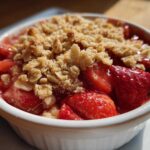 Close-up of a warm serving of Strawberry Rhubarb Crisp topped with golden oat crumble in a white ramekin.