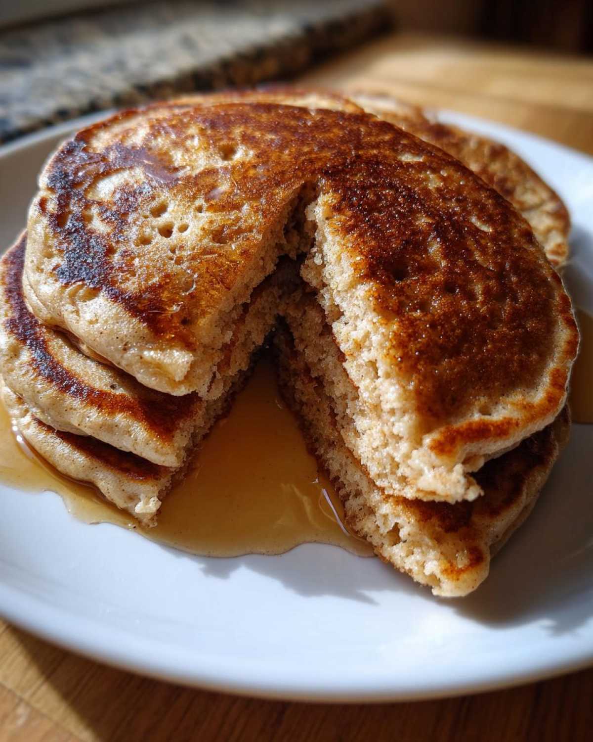 Close-up of a stack of golden brown Vegan Banana Oat Pancakes cut open, showing the fluffy interior and dripping maple syrup.